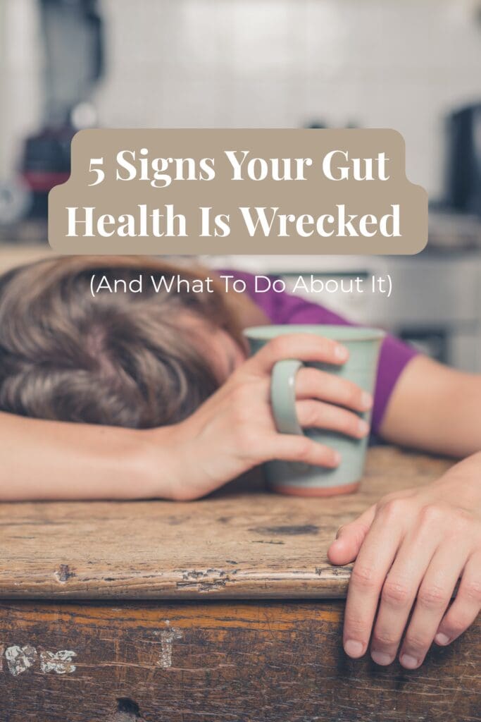 tired mom sitting at kitchen table with coffee with text overlay that reads 5 signs your gut health is wrecked